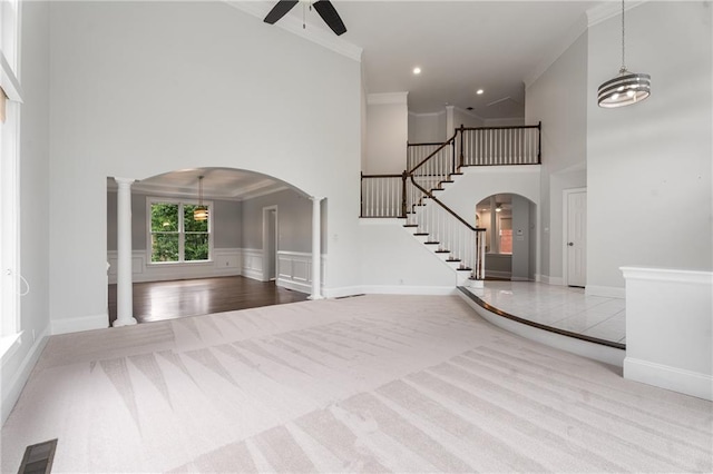 carpeted foyer entrance with arched walkways, ceiling fan, stairway, crown molding, and a towering ceiling