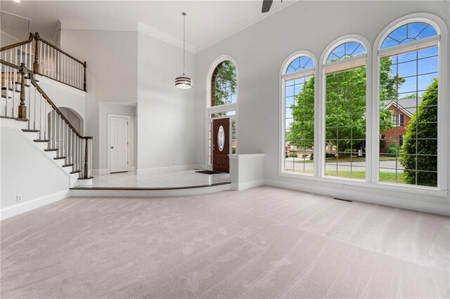 entryway with ornamental molding, a towering ceiling, carpet, and a healthy amount of sunlight