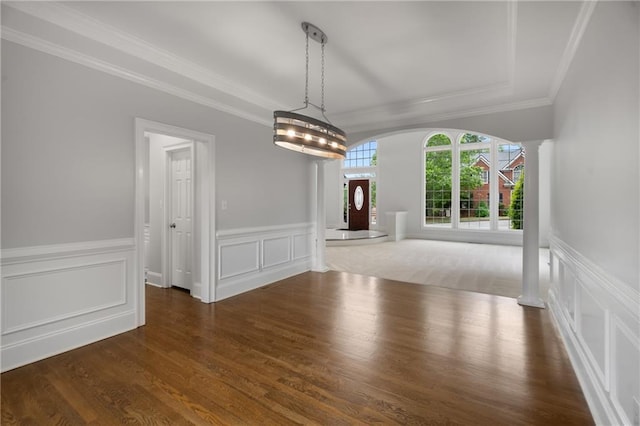 unfurnished dining area featuring wood finished floors, arched walkways, a decorative wall, ornamental molding, and ornate columns