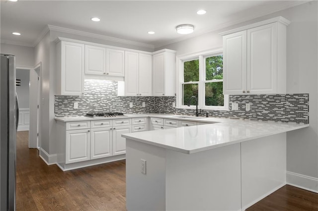 kitchen with appliances with stainless steel finishes, a sink, dark wood-style floors, a peninsula, and crown molding