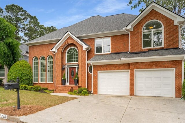 traditional-style house featuring a front yard, driveway, an attached garage, and brick siding
