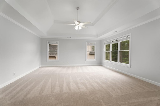 empty room with light colored carpet, a raised ceiling, ceiling fan, and baseboards
