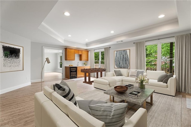 living area with light wood finished floors, recessed lighting, a tray ceiling, and baseboards