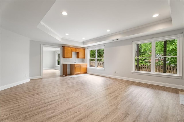unfurnished living room featuring light wood finished floors, recessed lighting, a tray ceiling, and baseboards