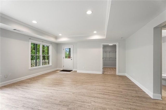 interior space with baseboards, visible vents, a raised ceiling, and light wood-style floors