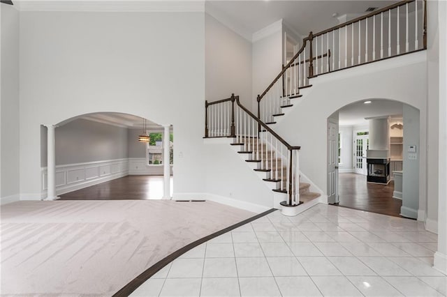 foyer featuring crown molding, a towering ceiling, arched walkways, and stairway