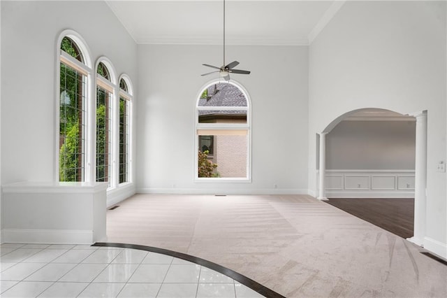 unfurnished dining area with arched walkways, carpet floors, ceiling fan, baseboards, and crown molding