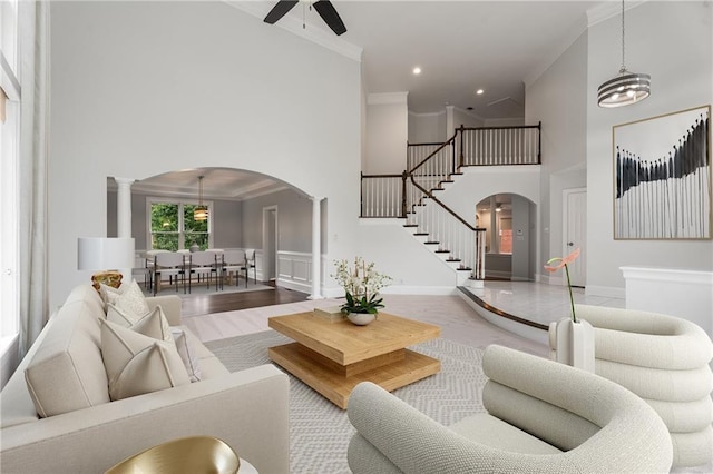 living room with crown molding, a ceiling fan, stairs, a towering ceiling, and arched walkways