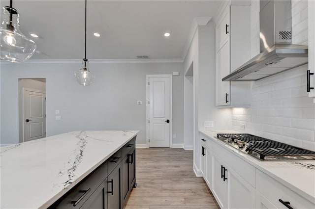 kitchen with wall chimney exhaust hood, light wood-type flooring, stainless steel gas stovetop, hanging light fixtures, and white cabinetry