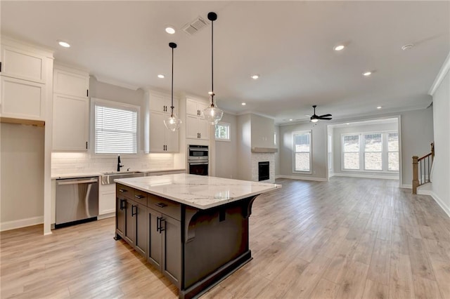 kitchen with light wood-type flooring, a center island, stainless steel appliances, white cabinetry, and decorative light fixtures