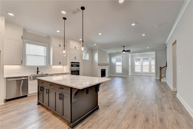 kitchen with a kitchen island, light wood-type flooring, hanging light fixtures, white cabinetry, and appliances with stainless steel finishes