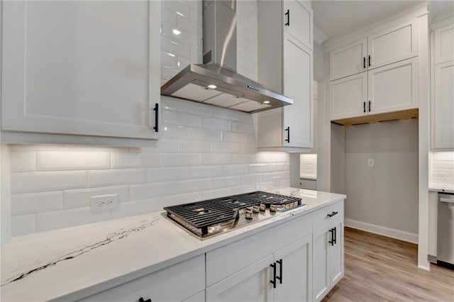 kitchen with wall chimney exhaust hood, light wood-type flooring, backsplash, white cabinets, and appliances with stainless steel finishes