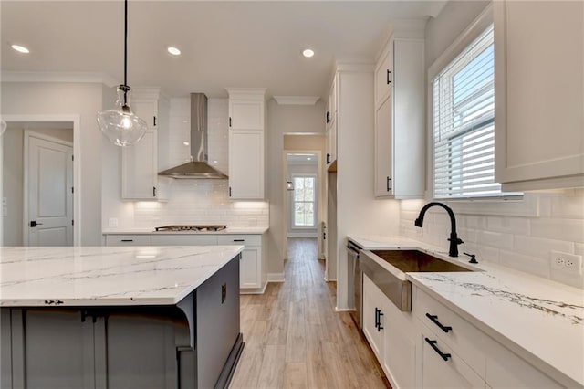 kitchen featuring wall chimney range hood, white cabinets, decorative light fixtures, and a healthy amount of sunlight