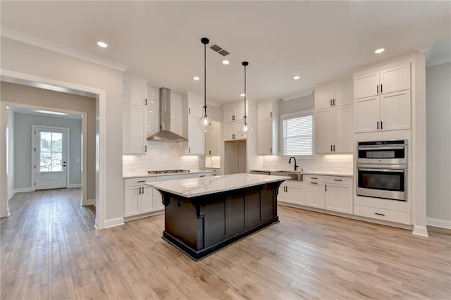 kitchen featuring a kitchen island, wall chimney exhaust hood, crown molding, and white cabinets