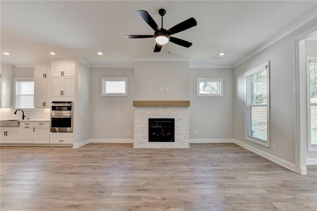 unfurnished living room with ceiling fan, sink, a fireplace, light wood-type flooring, and crown molding