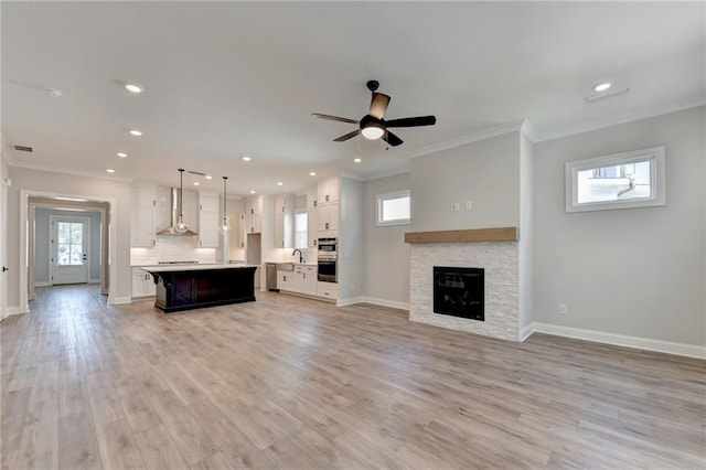 unfurnished living room featuring a fireplace, ornamental molding, light wood-type flooring, and ceiling fan