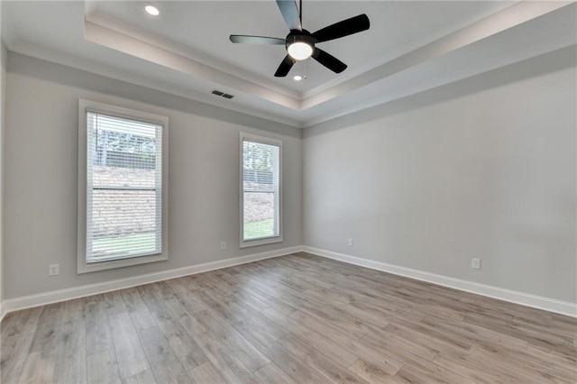 empty room featuring ceiling fan, light hardwood / wood-style floors, a tray ceiling, and a healthy amount of sunlight