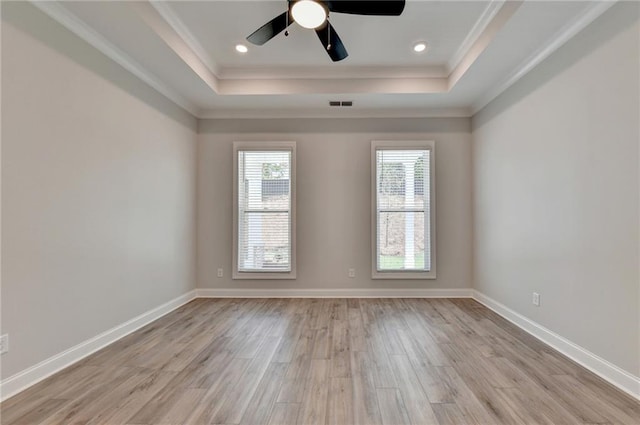 empty room with crown molding, ceiling fan, a tray ceiling, and light hardwood / wood-style floors