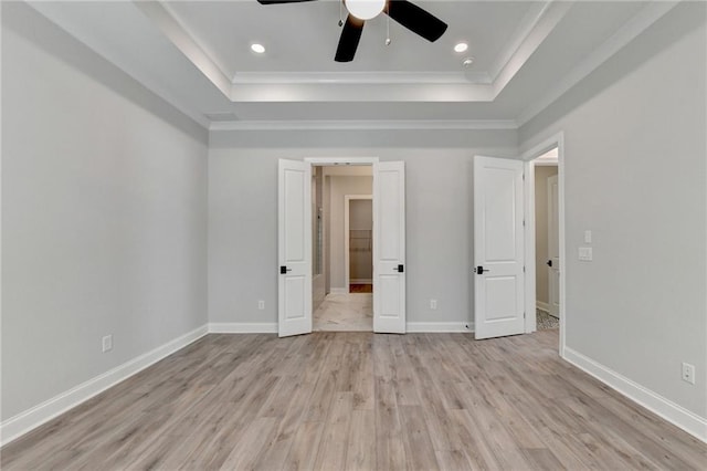 unfurnished bedroom featuring light hardwood / wood-style floors, a tray ceiling, crown molding, and ceiling fan