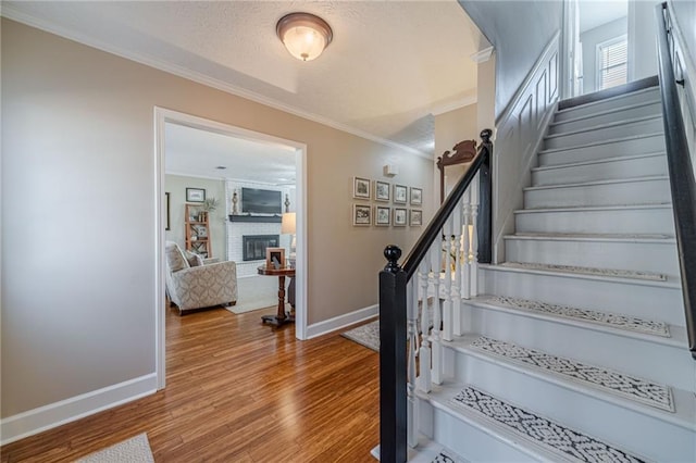 staircase with a fireplace, wood finished floors, crown molding, and a textured ceiling