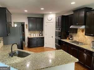 kitchen featuring sink, backsplash, light stone countertops, black gas stovetop, and stainless steel oven