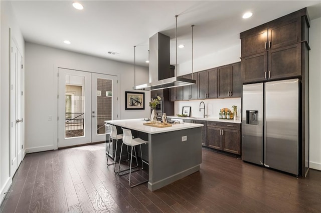 kitchen with a center island, island exhaust hood, pendant lighting, a kitchen bar, and appliances with stainless steel finishes