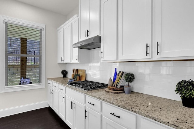 kitchen featuring stainless steel gas stovetop, white cabinets, tasteful backsplash, dark wood-type flooring, and light stone counters