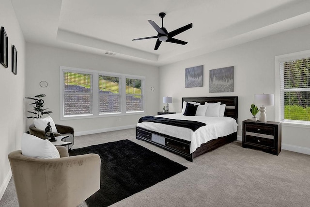 bedroom featuring ceiling fan, light colored carpet, and a raised ceiling