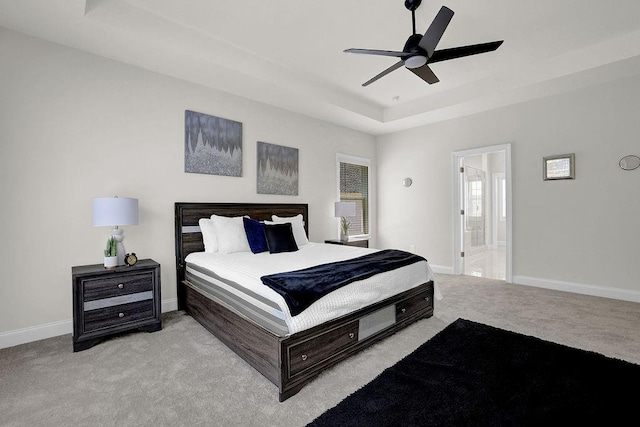 bedroom with ceiling fan, a raised ceiling, light colored carpet, and ensuite bath