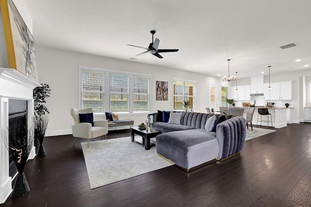 living room with ceiling fan with notable chandelier and dark hardwood / wood-style flooring