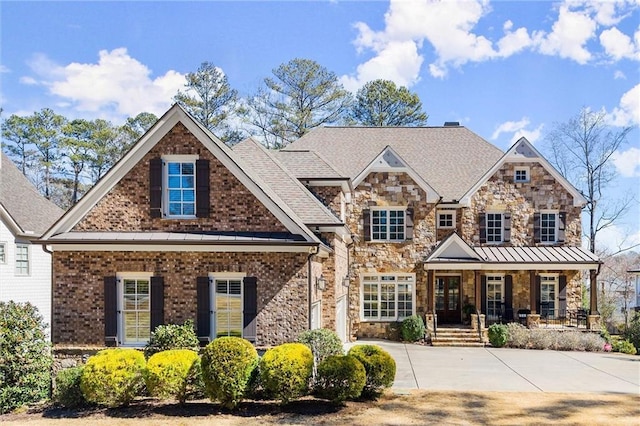 view of front of property with metal roof, covered porch, driveway, stone siding, and a standing seam roof