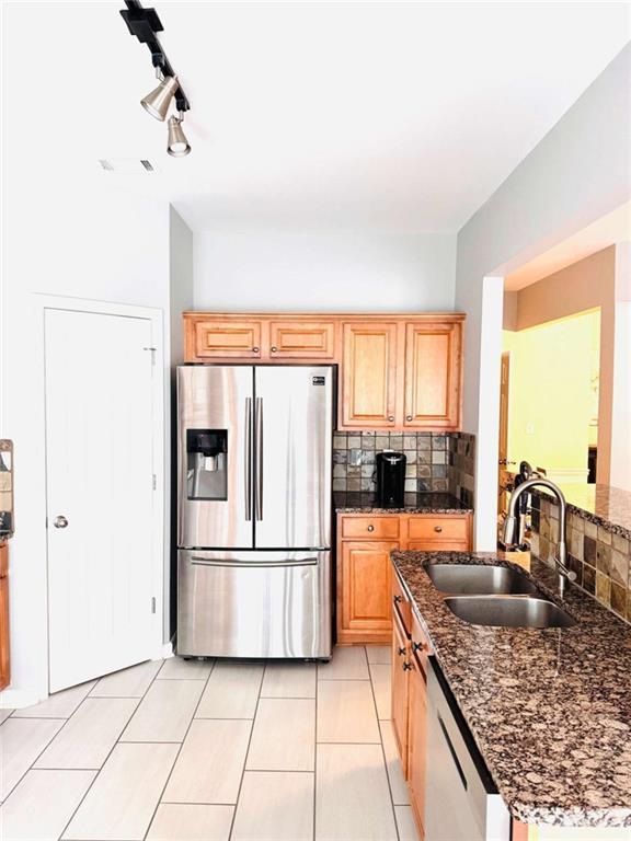 kitchen featuring sink, light tile patterned floors, stainless steel fridge with ice dispenser, and dark stone counters