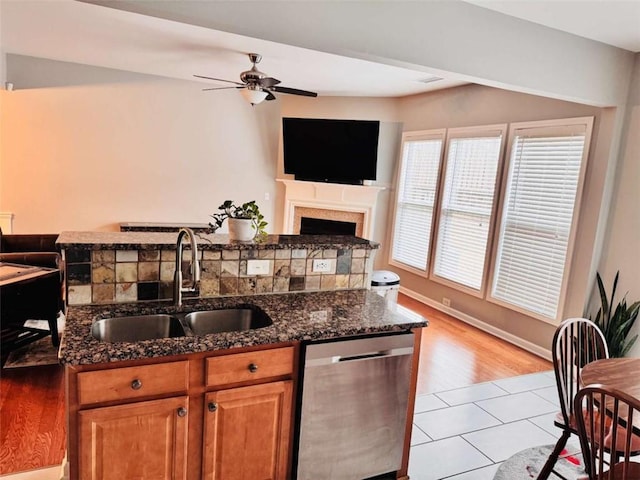 kitchen featuring dishwasher, dark stone countertops, sink, ceiling fan, and light tile patterned floors