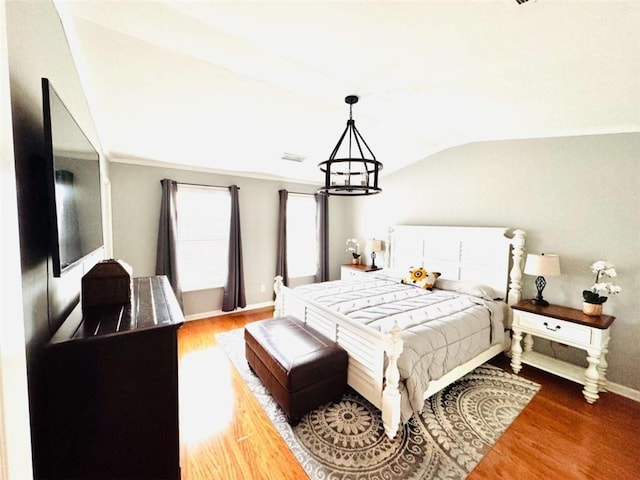 bedroom with wood-type flooring, lofted ceiling, and a chandelier