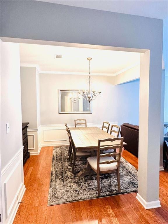 dining room with wood-type flooring, an inviting chandelier, and crown molding