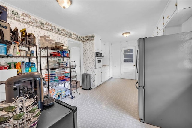 kitchen featuring white oven, freestanding refrigerator, light floors, ornamental molding, and white cabinetry