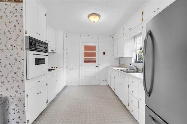 kitchen with a sink, light countertops, white cabinets, freestanding refrigerator, and oven