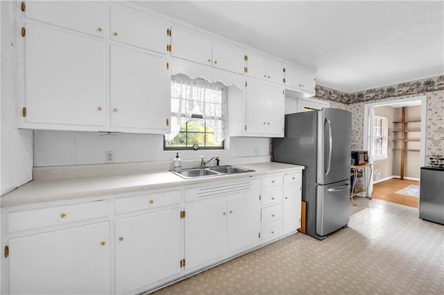 kitchen featuring freestanding refrigerator, a sink, and white cabinetry