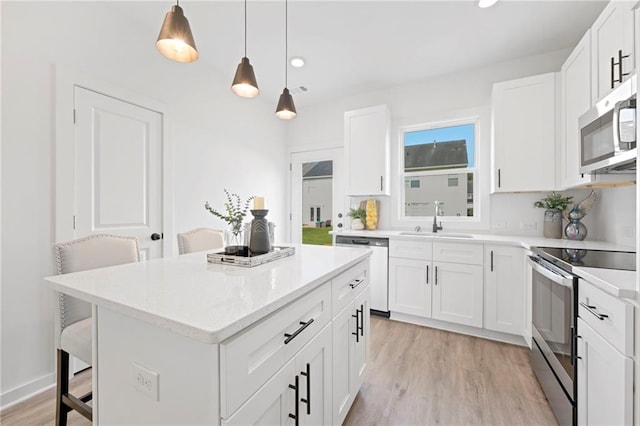 kitchen featuring light wood-style flooring, stainless steel appliances, a kitchen island, a sink, and a kitchen bar