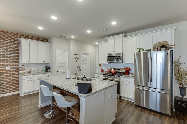 kitchen with visible vents, dark wood-style floors, brick wall, stainless steel appliances, and a sink