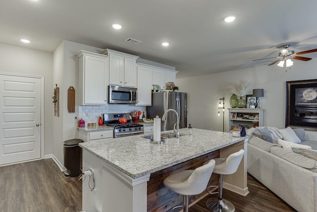 kitchen featuring stainless steel appliances, a sink, open floor plan, backsplash, and dark wood-style floors