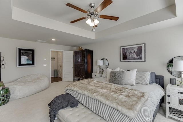 bedroom featuring visible vents, a raised ceiling, a ceiling fan, and light colored carpet