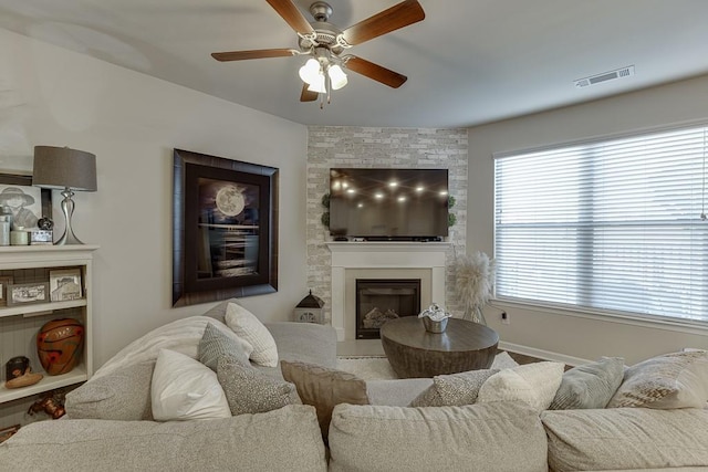 living area with a large fireplace, ceiling fan, and visible vents