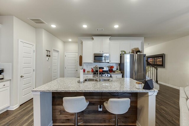 kitchen featuring visible vents, dark wood-style floors, a sink, stainless steel appliances, and backsplash