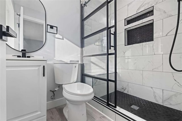 bathroom with hardwood / wood-style flooring, tiled shower, vanity, and toilet