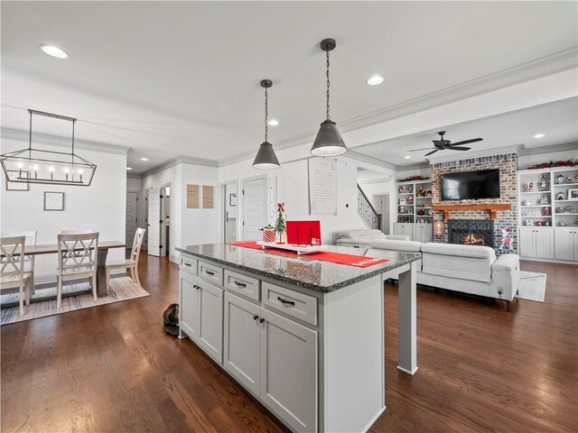 kitchen with a brick fireplace, dark hardwood / wood-style floors, dark stone counters, decorative light fixtures, and ornamental molding