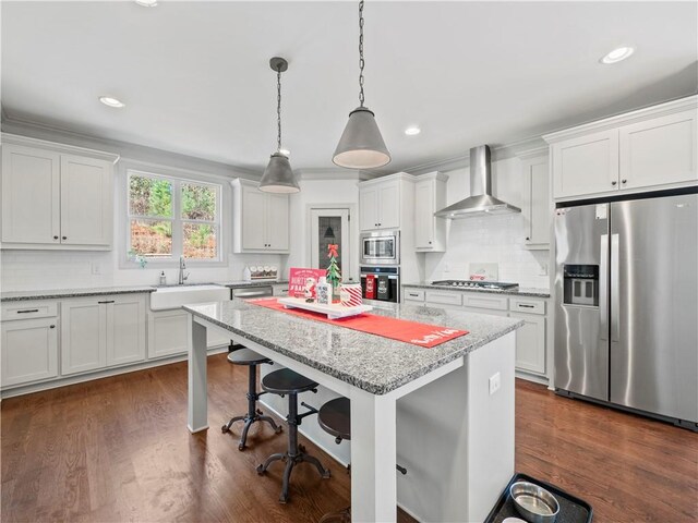 kitchen with sink, wall chimney exhaust hood, appliances with stainless steel finishes, dark hardwood / wood-style flooring, and white cabinetry