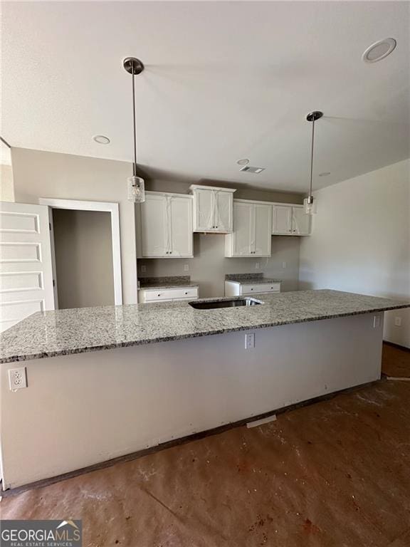 kitchen with white cabinetry, light stone countertops, a large island with sink, and pendant lighting