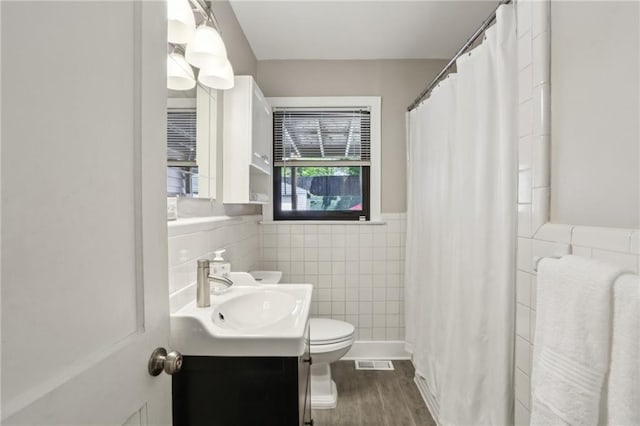 bathroom with tile walls, toilet, vanity, wainscoting, and wood finished floors