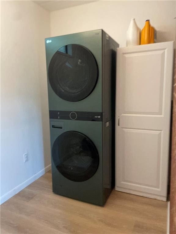 laundry area with stacked washer / drying machine, light wood-type flooring, and baseboards